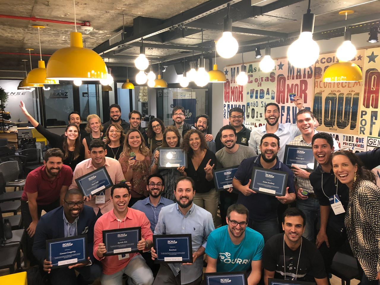 Foto com todos os participantes do programa. Eles estão segurando certificados. O ambiente é colorido e iluminado.