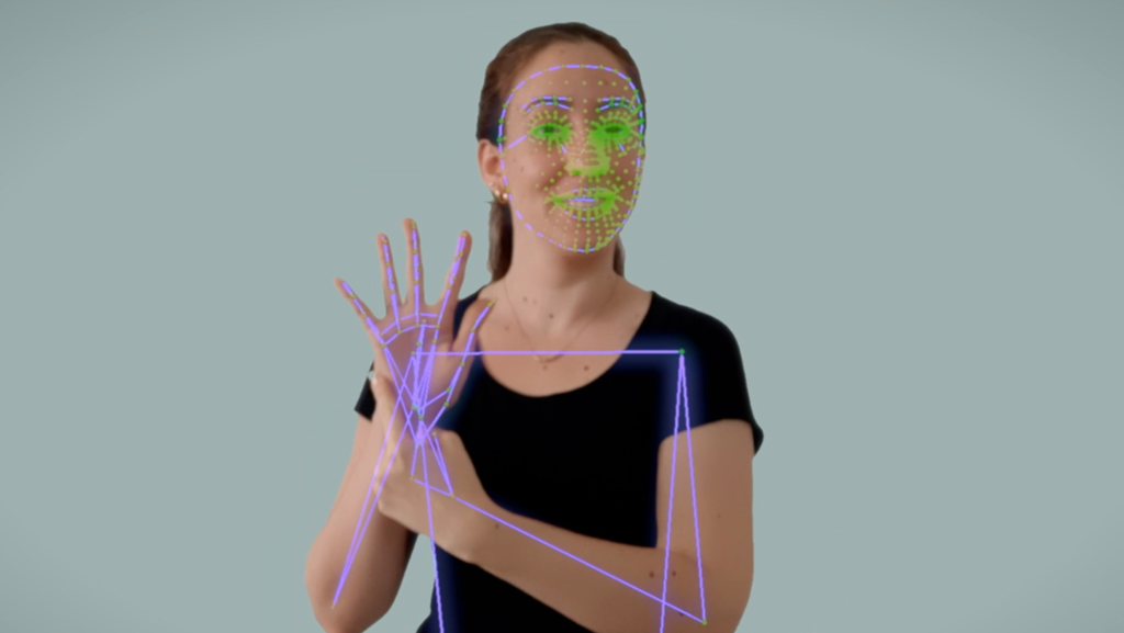 Demonstração da tecnologia inovadora de reconhecimento dos movimentos feito pela inteligência artificial, com a imagem de uma mulher branca usando língua de sinal e marcações no rosto e nas mãos feitos pela IA.