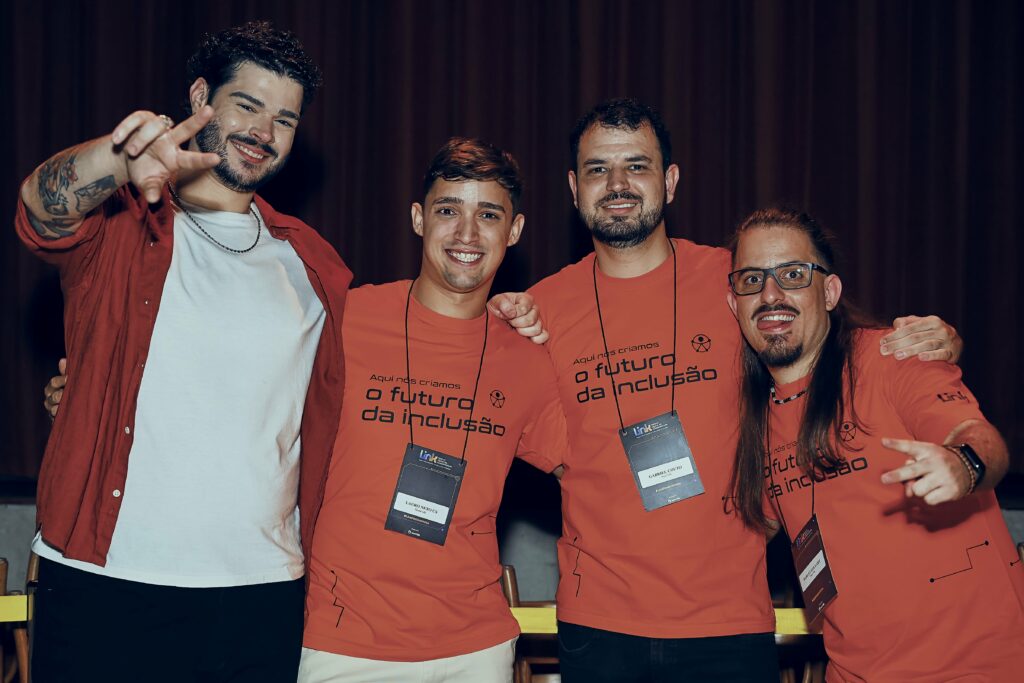 Foto de Lauro Neto sorrindo, ao lado de três Hand Talkers, que tambem estão sorrindo.